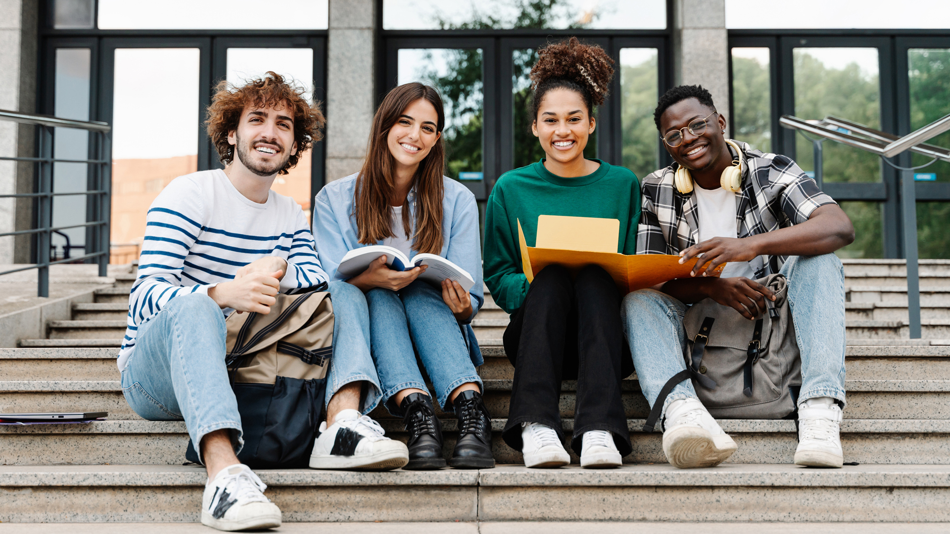 four students sitting on stairs smiling at the camera